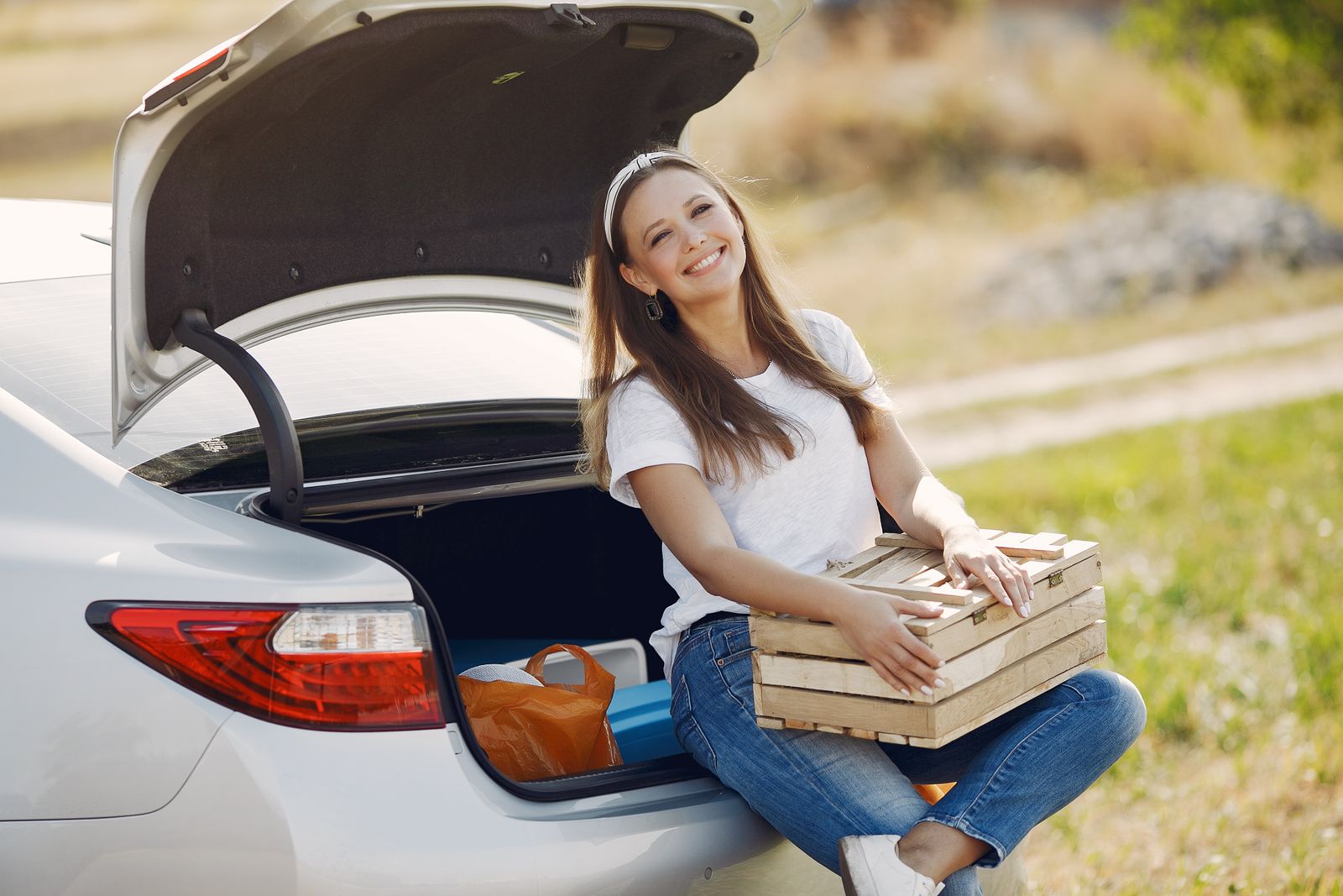 A traveler with a box beside an open car trunk during a countryside road trip.